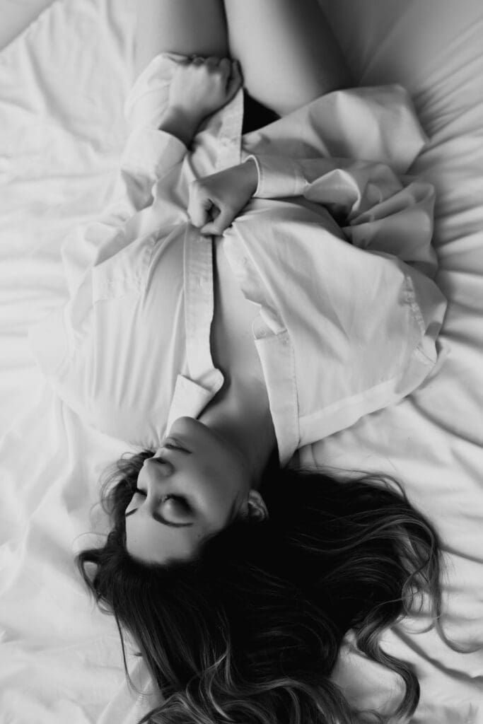 upside down image of a woman laying in bed in her white button up and lingerie for her boudoir photoshoot