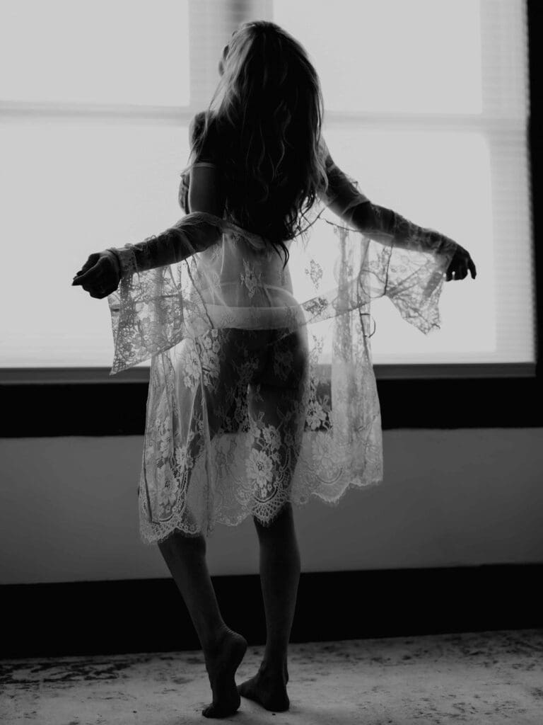 woman in front of a window twirling in a sheer robe for her bridal boudoir photoshoot