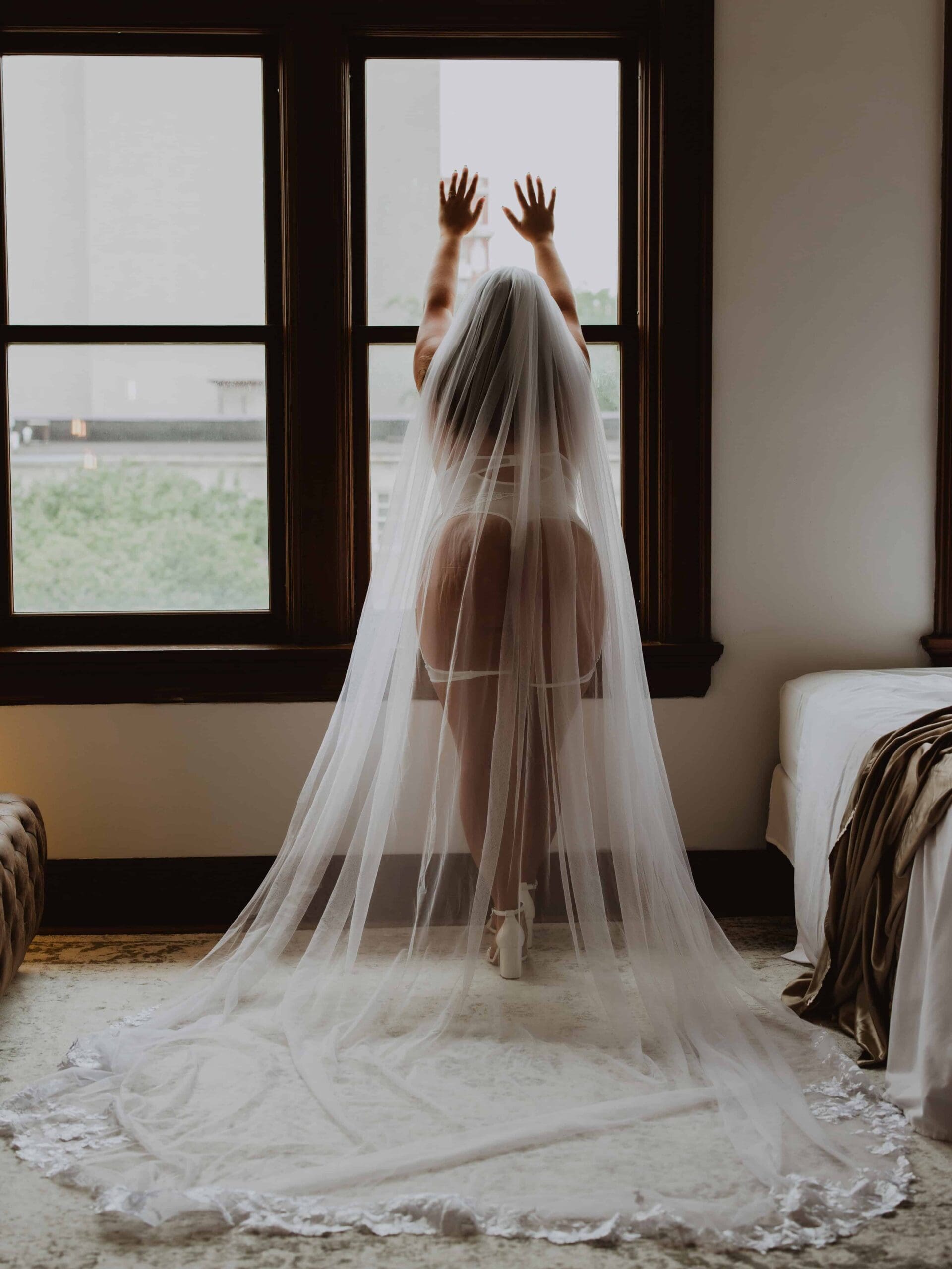woman wearing a long veil posing by the window in her boudoir photoshoot