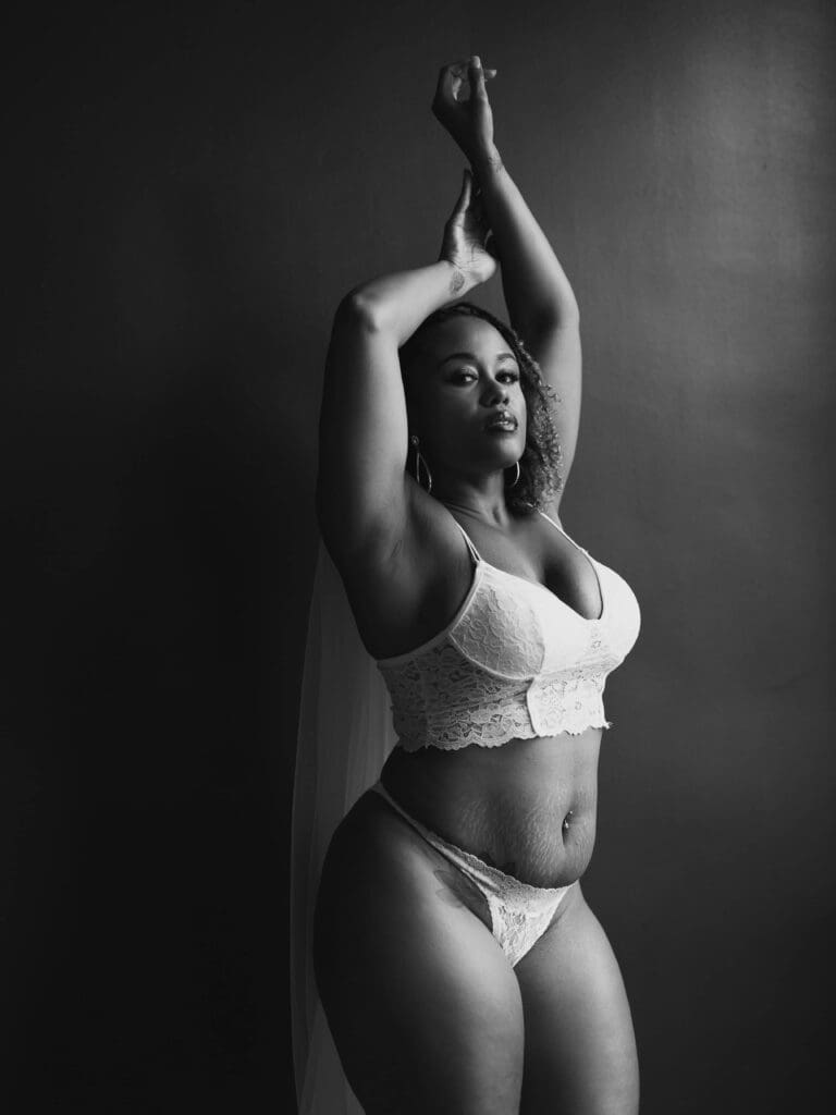 woman in her veil and white bridal outfit with arms up posing at her boudoir session